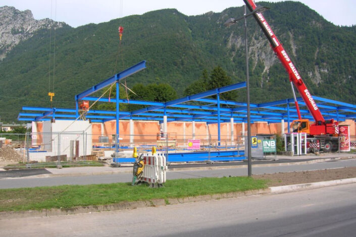 Baustelle mit blauer Stahlkonstruktion für den Neubau eines Einkaufscenters vor Bergkulisse
