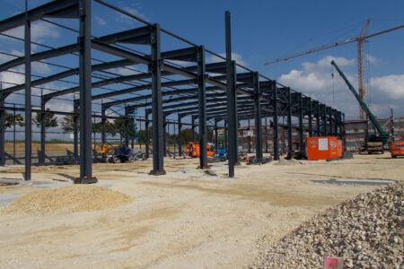 Stahlkonstruktion einer Produktionshalle im Rohbau mit Kran und Baumaschinen