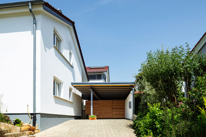 Moderner Carport mit Holzverkleidung und Schiebetür neben einem Einfamilienhaus