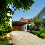 Moderner Carport mit Holzverkleidung und Schiebetür neben einem Einfamilienhaus