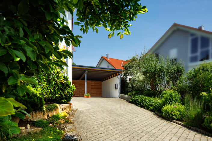 Moderner Carport mit Holzverkleidung und Schiebetür neben einem Einfamilienhaus