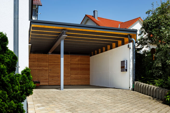 Carport mit sichtbarer Stahlkonstruktion, Holzverkleidung und seitlicher Betonwand