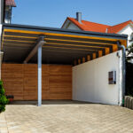 Carport mit sichtbarer Stahlkonstruktion, Holzverkleidung und seitlicher Betonwand