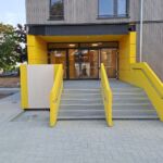 Zwei Außentreppen mit gelber Stahlblechverkleidung und Edelstahlhandläufen vor einem Eingang