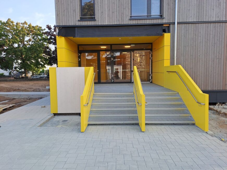 Zwei Außentreppen mit gelber Stahlblechverkleidung und Edelstahlhandläufen vor einem Eingang