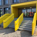 Zwei freistehende Außentreppen mit gelber Stahlblechverkleidung und Edelstahlhandlauf