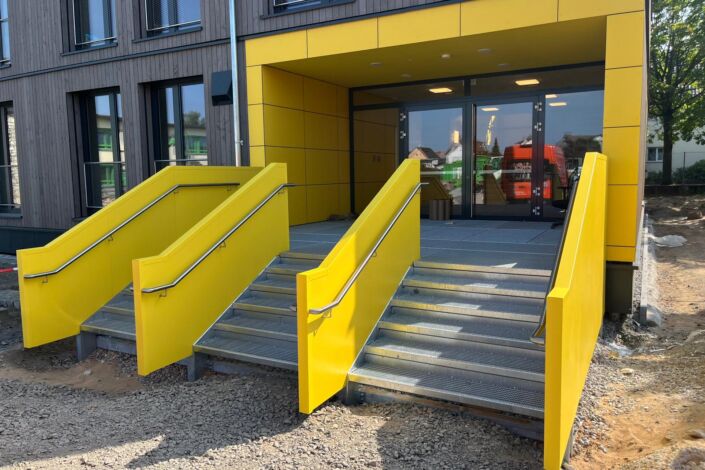 Zwei freistehende Außentreppen mit gelber Stahlblechverkleidung und Edelstahlhandlauf