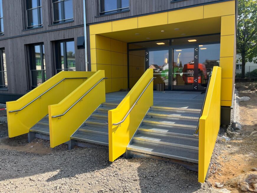 Zwei freistehende Außentreppen mit gelber Stahlblechverkleidung und Edelstahlhandlauf