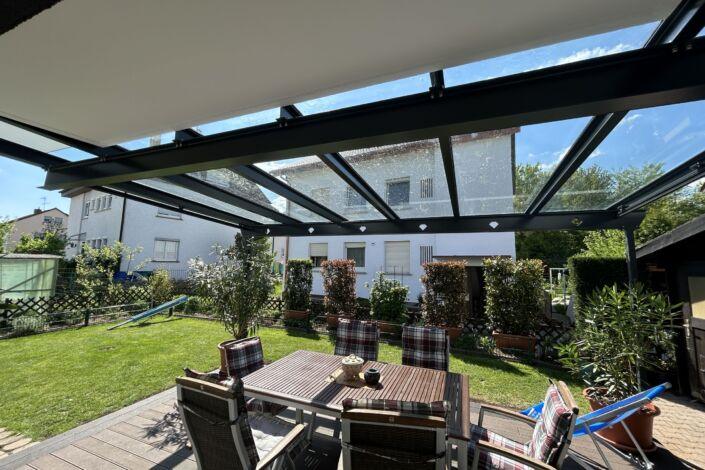 Ausblick unter einer Terrassenüberdachung mit Glasdach auf Garten mit Sitzbereich