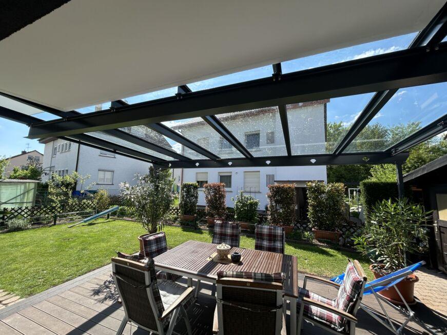 Ausblick unter einer Terrassenüberdachung mit Glasdach auf Garten mit Sitzbereich