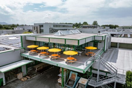 Luftaufnahme des modernen Kantinenanbaus mit Terrasse, Sonnenschirmen und Stahlkonstruktion von Stahlbau Nägele