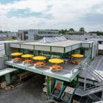 Luftaufnahme des modernen Kantinenanbaus mit Terrasse, Sonnenschirmen und Stahlkonstruktion von Stahlbau Nägele