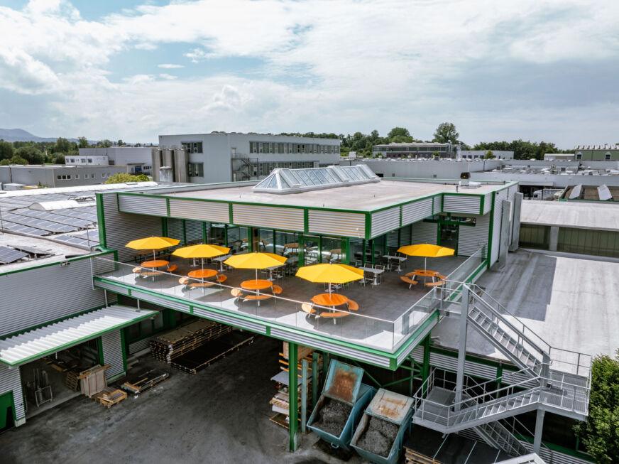 Luftaufnahme des modernen Kantinenanbaus mit Terrasse, Sonnenschirmen und Stahlkonstruktion von Stahlbau Nägele