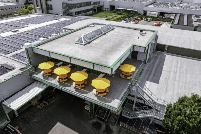 Dachaufsicht auf den Kantinenanbau mit Terrasse und gelben Sonnenschirmen – realisiert durch Stahlbau Nägele