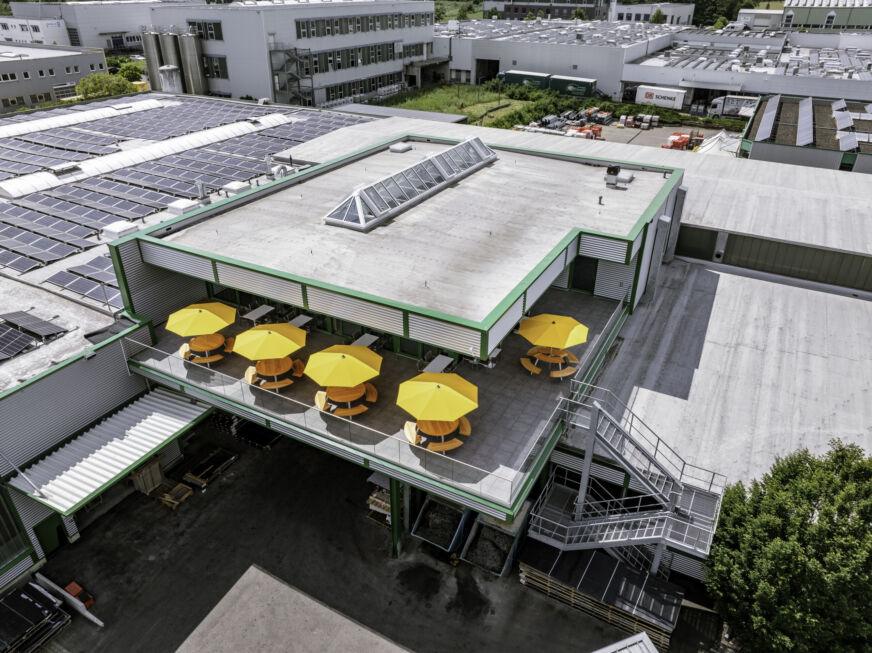 Dachaufsicht auf den Kantinenanbau mit Terrasse und gelben Sonnenschirmen – realisiert durch Stahlbau Nägele