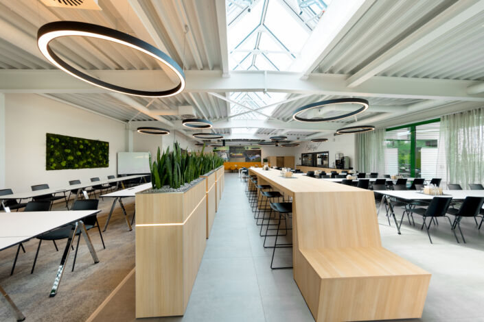 Moderne Kantine mit zentraler Sitzinsel, natürlicher Belichtung und stilvoller Holzverkleidung – Stahlbau Nägele