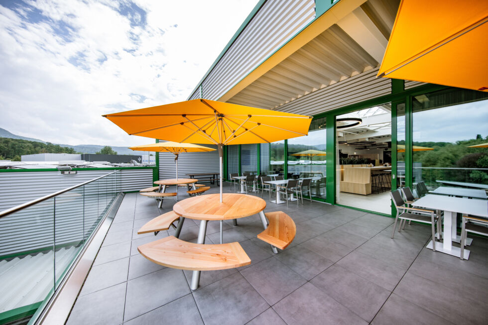Moderne Dachterrasse mit Holztischen und gelben Sonnenschirmen vor der neuen Betriebskantine – Stahlbau Nägele