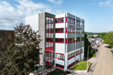 Aufgestocktes Firmengebäude mit Stahl-Verbindungsbau und rotem Fensterrahmen
