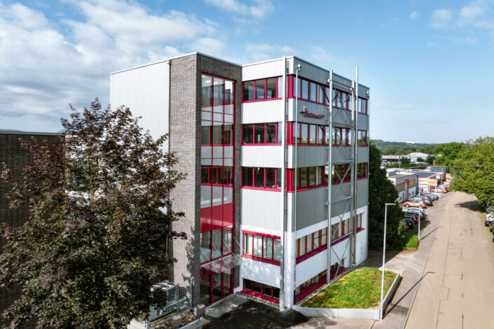 Aufgestocktes Firmengebäude mit Stahl-Verbindungsbau und rotem Fensterrahmen