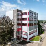 Aufgestocktes Firmengebäude mit Stahl-Verbindungsbau und rotem Fensterrahmen