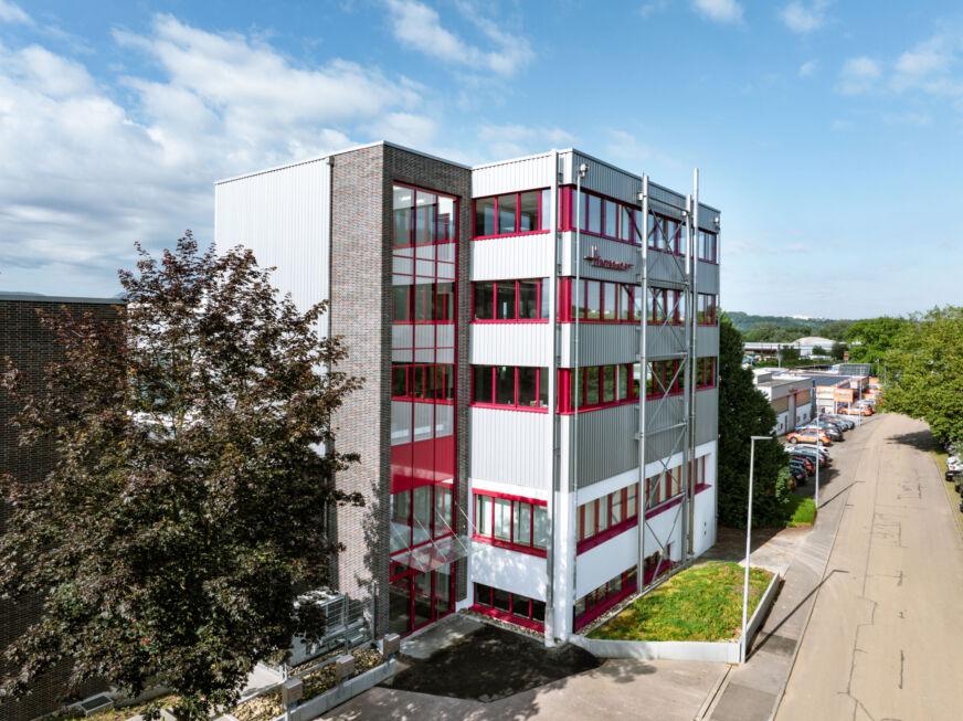 Aufgestocktes Firmengebäude mit Stahl-Verbindungsbau und rotem Fensterrahmen