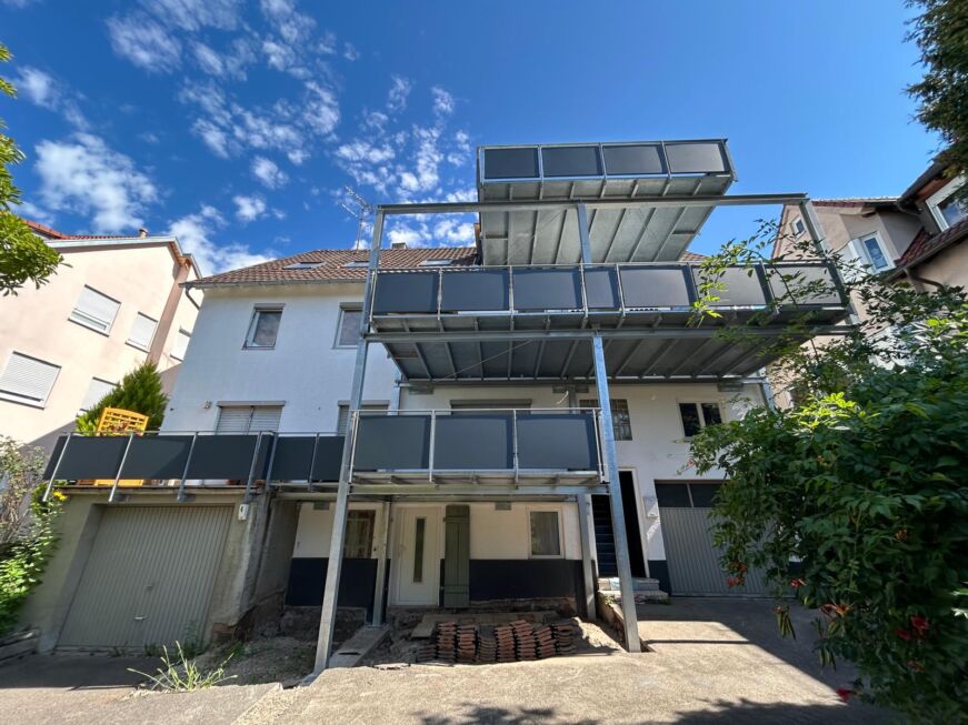 Dreigeschossiger Stahlbalkon mit grauen Füllungen vor einem Wohnhaus mit Flachdach und Garagen