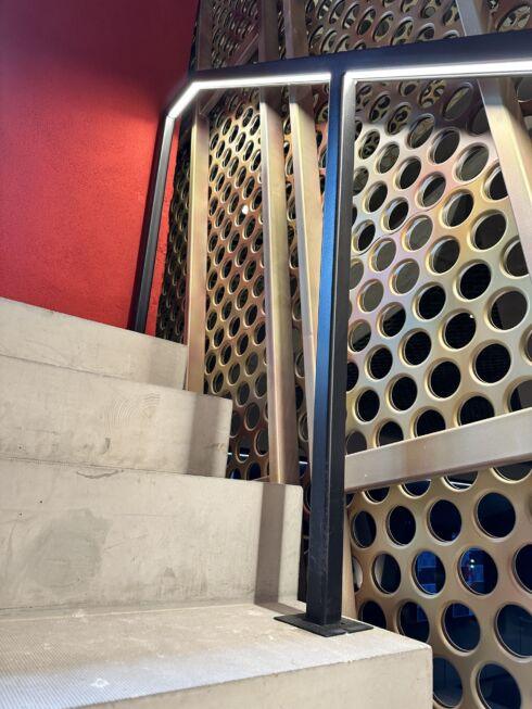 Treppenaufgang mit quadratischem LED-Handlauf und gelochter Metallverkleidung in der MHP-Arena