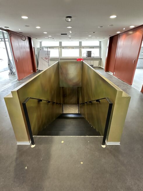 Treppenabgang mit pulverbeschichteten Handläufen und goldfarbener Wandverkleidung in der MHP-Arena