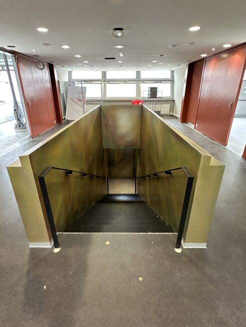 Treppenabgang mit pulverbeschichteten Handläufen und goldfarbener Wandverkleidung in der MHP-Arena