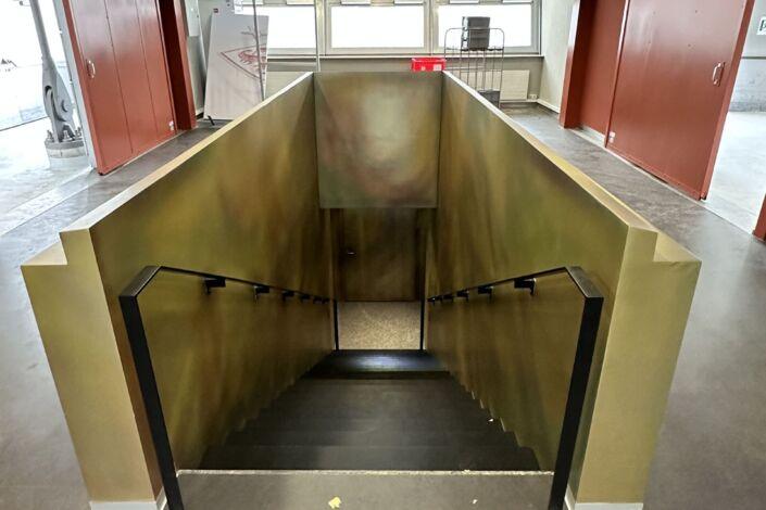 Treppenabgang mit pulverbeschichteten Handläufen und goldfarbener Wandverkleidung in der MHP-Arena