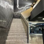 Treppe mit Flachstahl-Handläufen und dunkler Wandverkleidung in der MHP-Arena, beleuchtet durch moderne Lichtinstallation