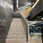 Treppe mit Flachstahl-Handläufen und dunkler Wandverkleidung in der MHP-Arena, beleuchtet durch moderne Lichtinstallation