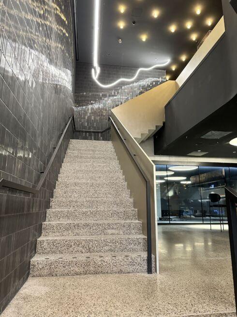 Treppe mit Flachstahl-Handläufen und dunkler Wandverkleidung in der MHP-Arena, beleuchtet durch moderne Lichtinstallation