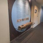 Seitliche Ansicht des historischen Teuchels aus dem „heilsamen Bad zu Boll“ im Foyer des Kurhauses Bad Boll. Das Holzstück liegt auf einer gebogenen Rundstahl-Unterkonstruktion, gefertigt von Stahlbau Nägele.